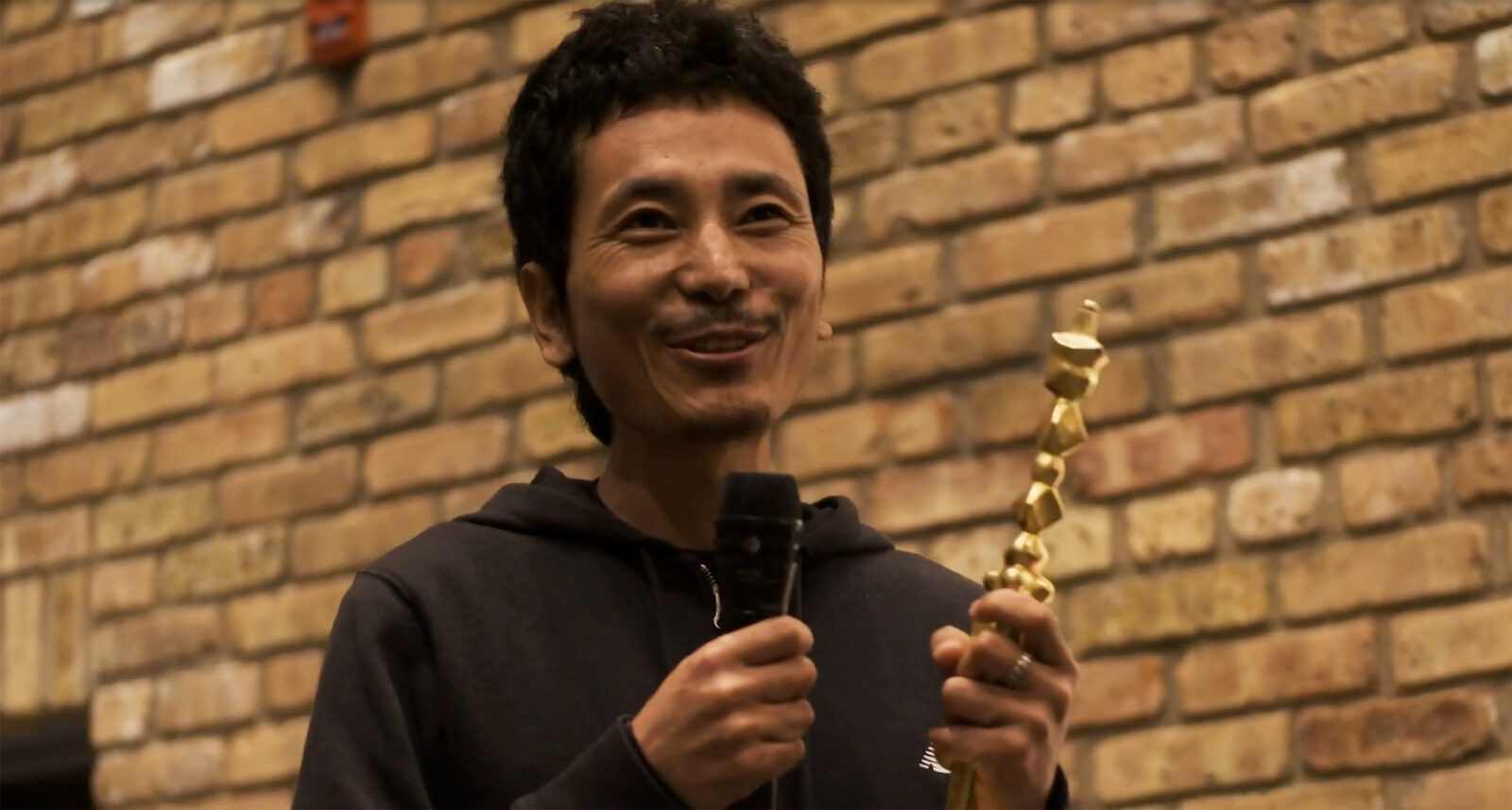 artist tenzin gyurmey holding the rubin art prize and speaking into a microphone