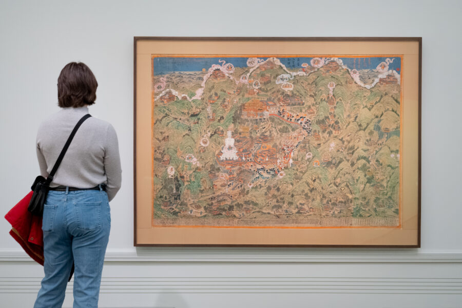 an adult stands with their back towards the viewer in front of the Panoramic Map of Mount Wutai
