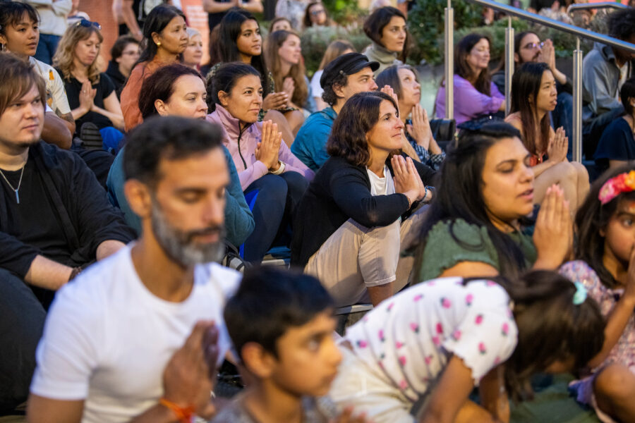 Group of people gathered close together and sitting with their hands placed in prayer in front of them.