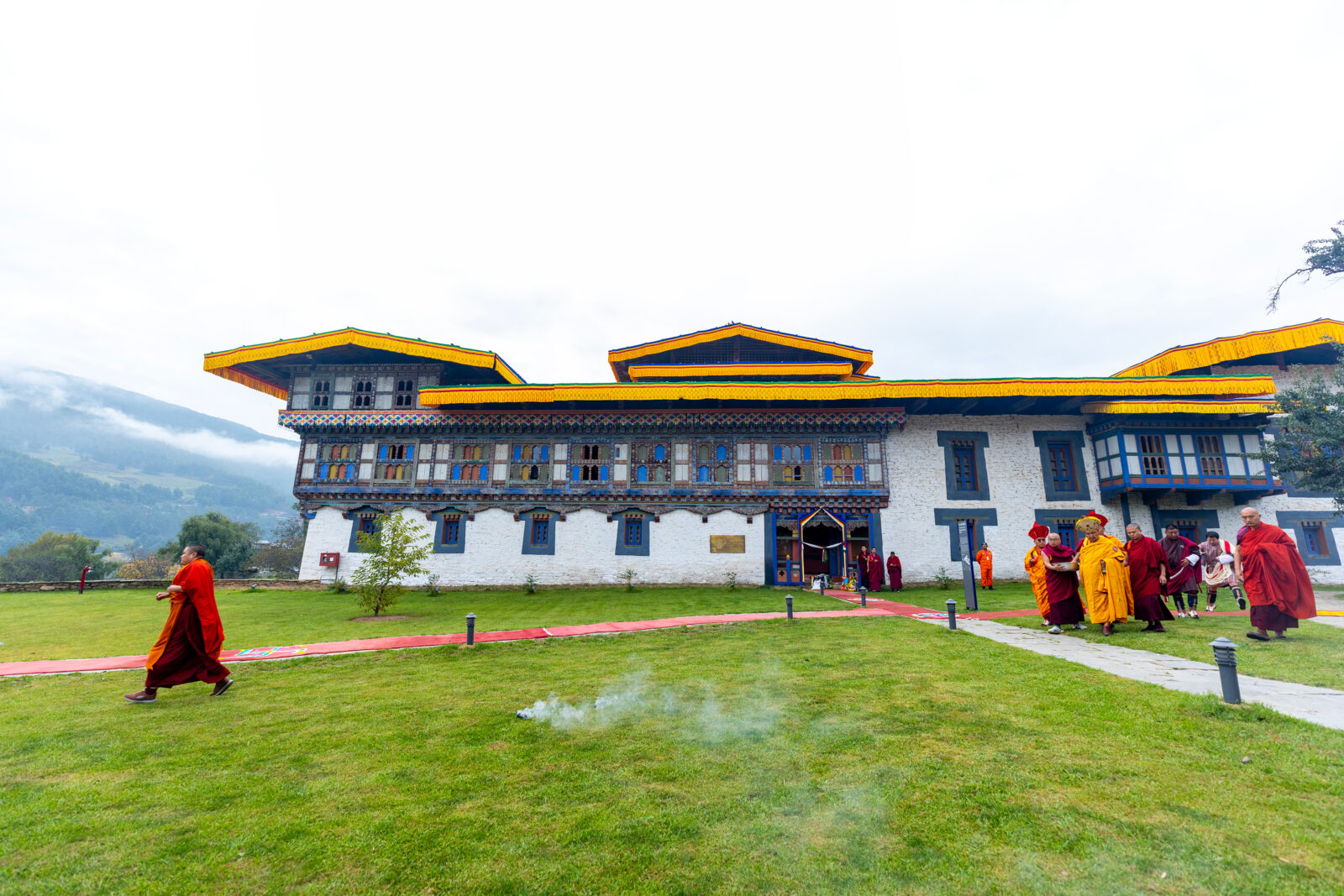 external view of the front of the Wangduechhoeling palace with monks walking in front on green grass