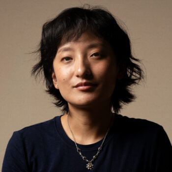 An adult woman with short black hair wearing a black shirt and a silver necklace