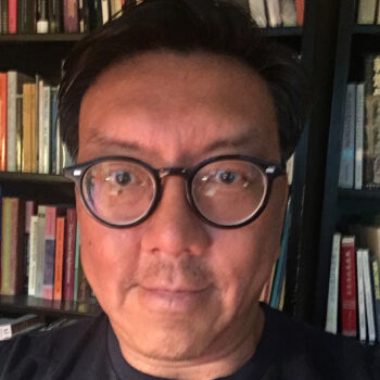 close-up of Winston Kyan wearing glasses and smiling in front of a bookshelf