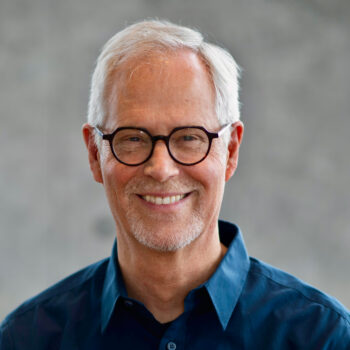a smiling adult man with gray hair wearing black glasses
