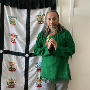 a man in a green traditional shirt standing with his finger tips together