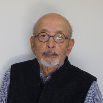 An adult man with a gray beard and mustache wearing black glasses, a black vest, and a blue button down shirt