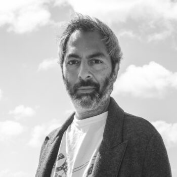 black and white photo of an adult man with a mustache and bear wearing a shirt and blazer