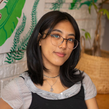 an adult woman with black hair smiling and wearing glasses
