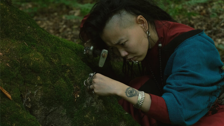 Adult woman crouching beside tree roots, holding a hammer in her right hand