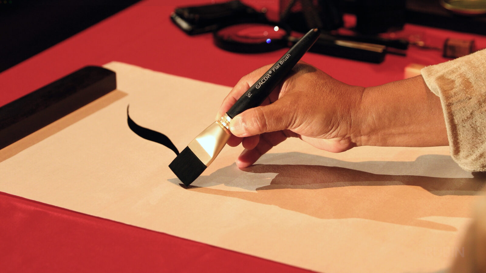 the hand of an artist holds a paintbrush to a piece of calligraphy paper