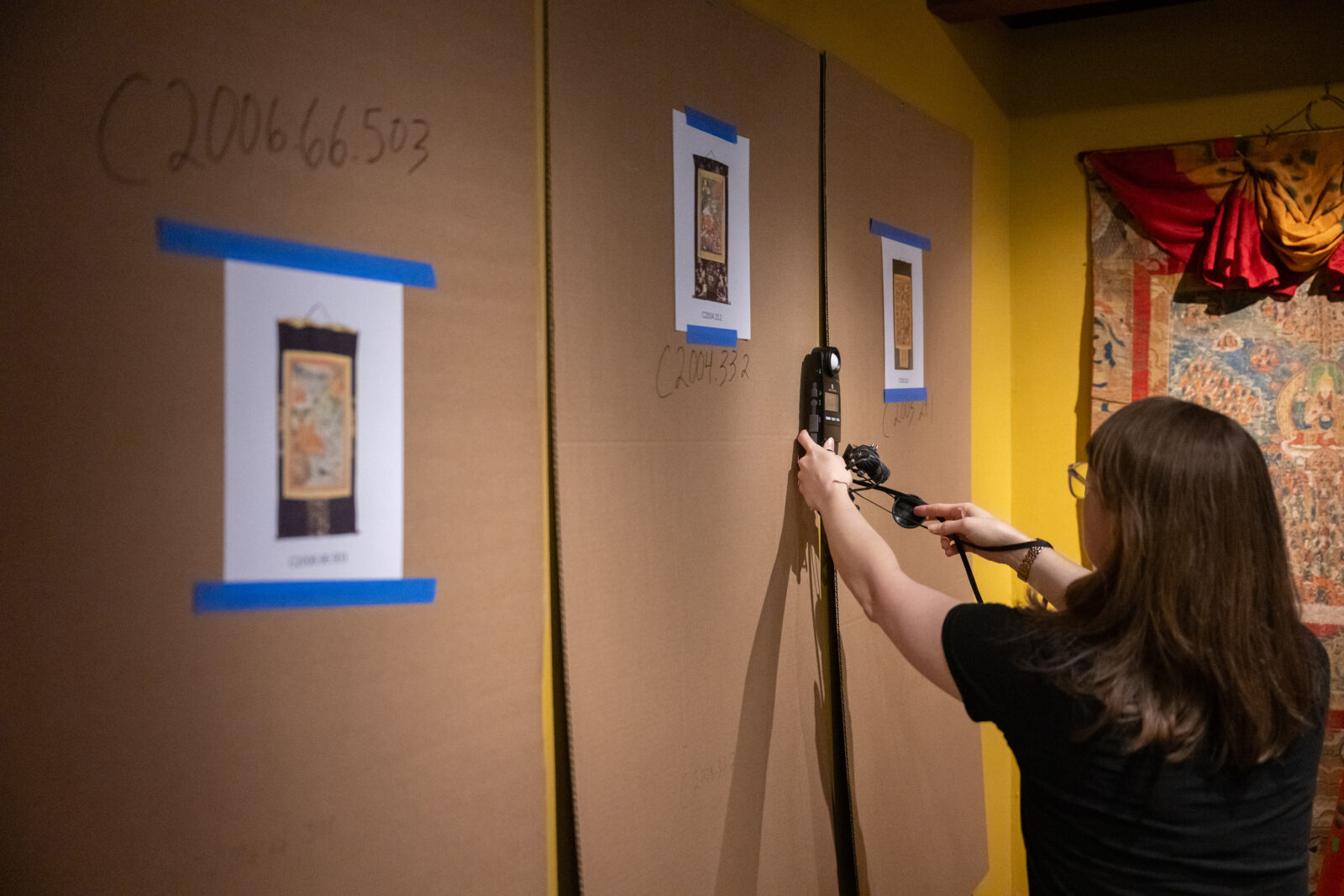 an art handler tests the light on a wall as they prepare to hang thangkas