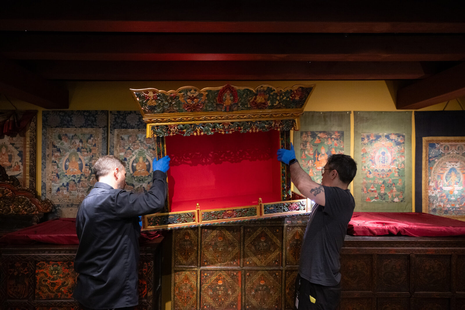 two art handlers lift the top of a shrine cabinet to place it for installation