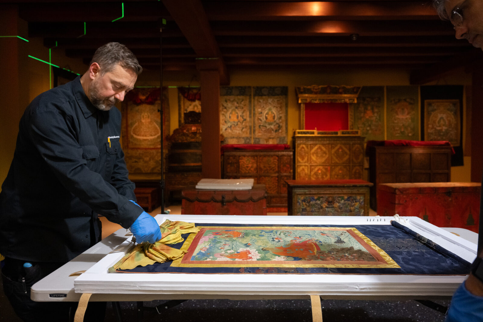 an art handler stands over a thangka painting in the Rubin Museum Tibetan Buddhist Shrine Room, preparing it for installation