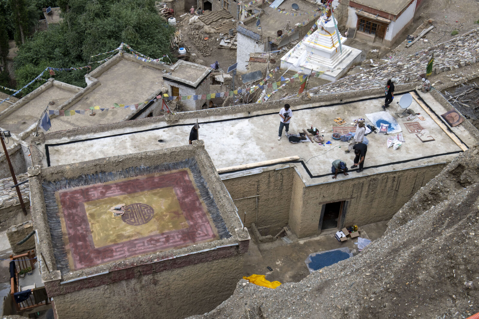An overhead view of six figures standing on a rooftop outlined by a black line, with pigment, stencils, and other art supplies scattered across the rooftop