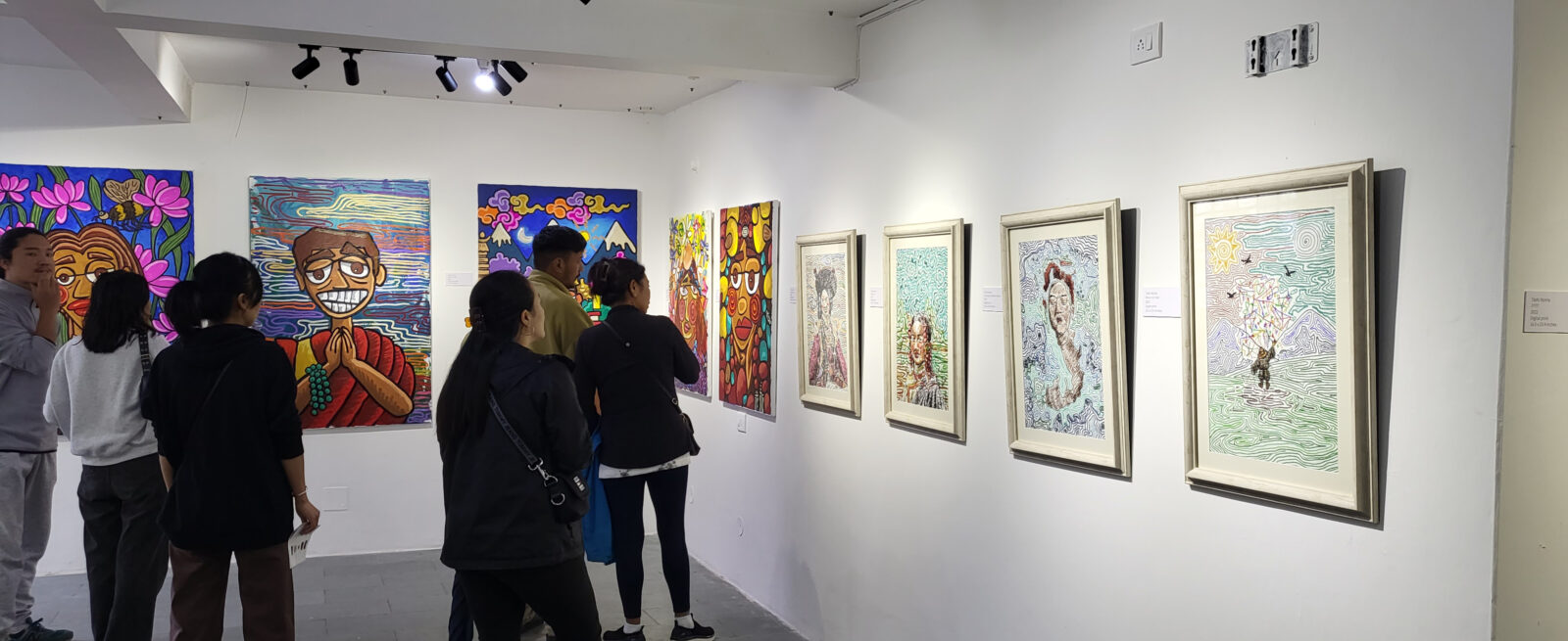 a group of people look at framed artwork and artwork on canvas hanging on white gallery walls