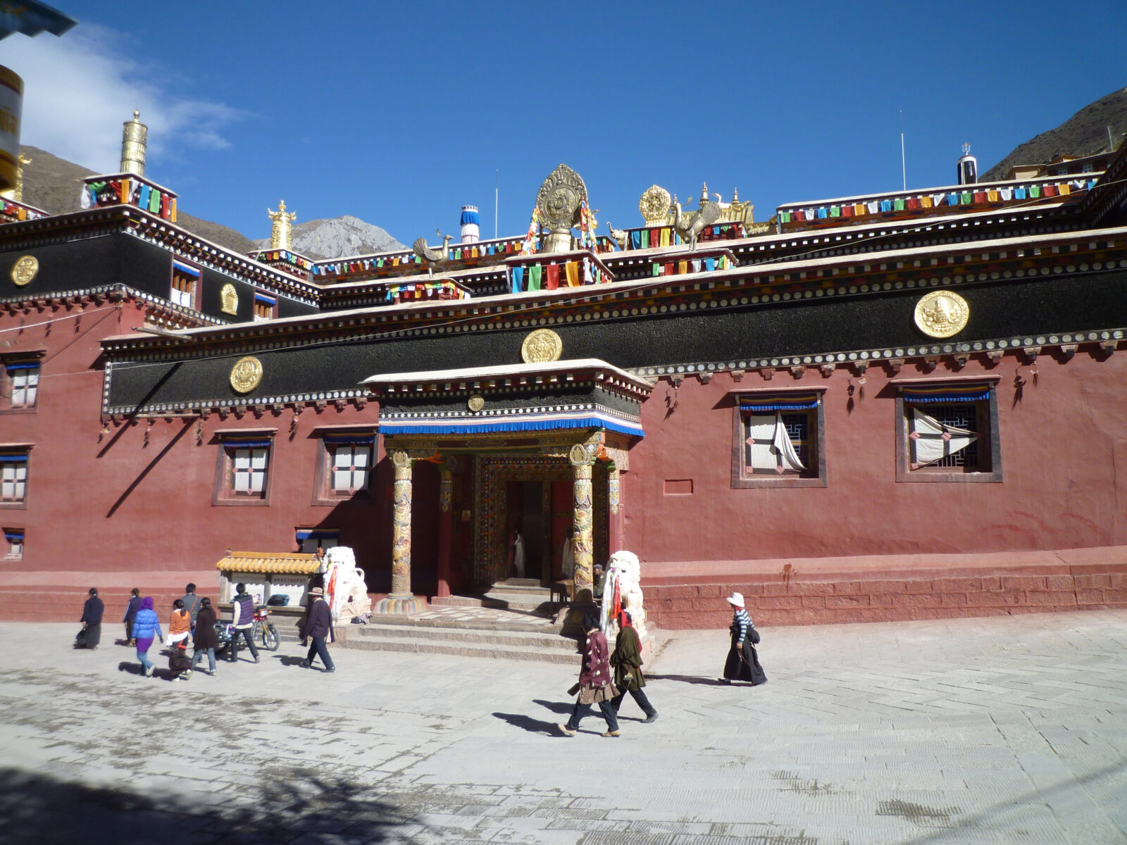 people walking in front of a brown building with multicolored flags along the trim