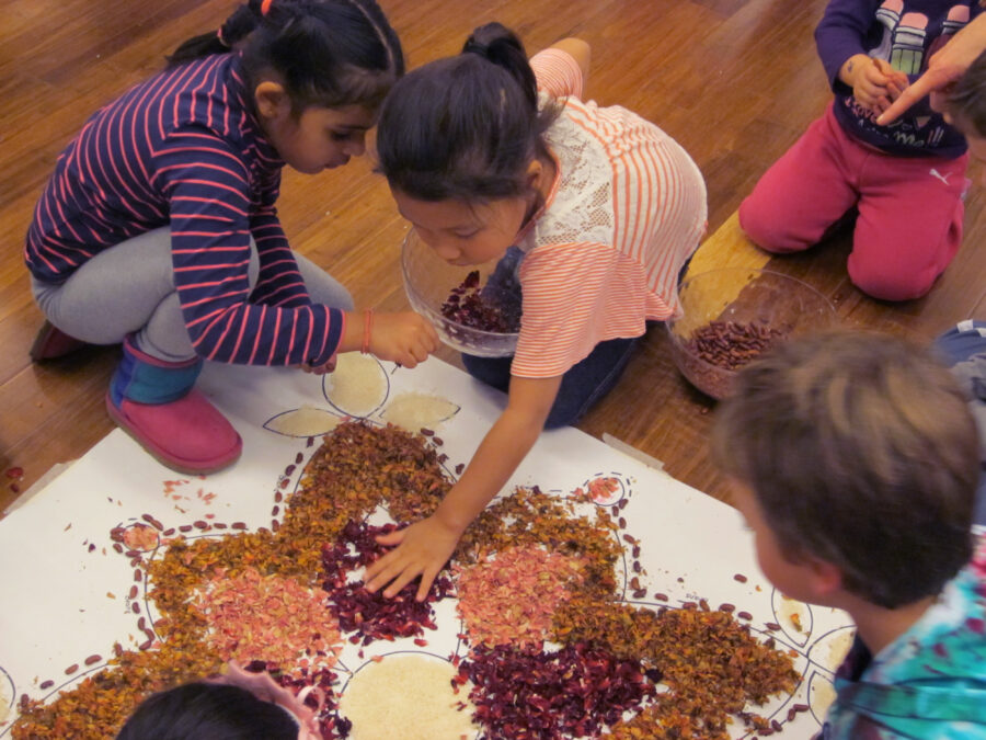 Four kids place pink, yellow, and purple flower petals on a white paper on the ground