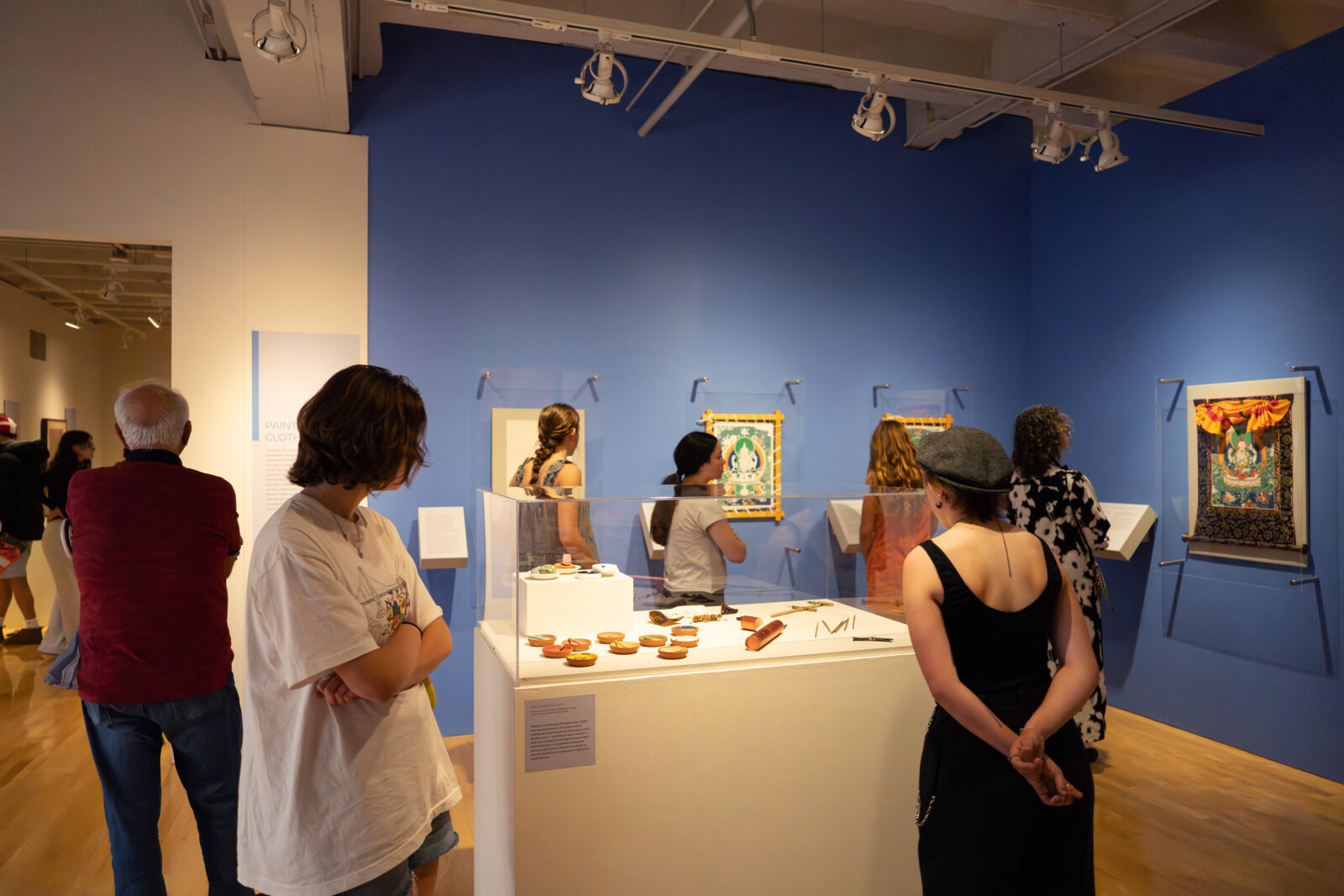 Visitors view paintings and objects displayed in a blue-walled gallery at the Flaten Art Museum
