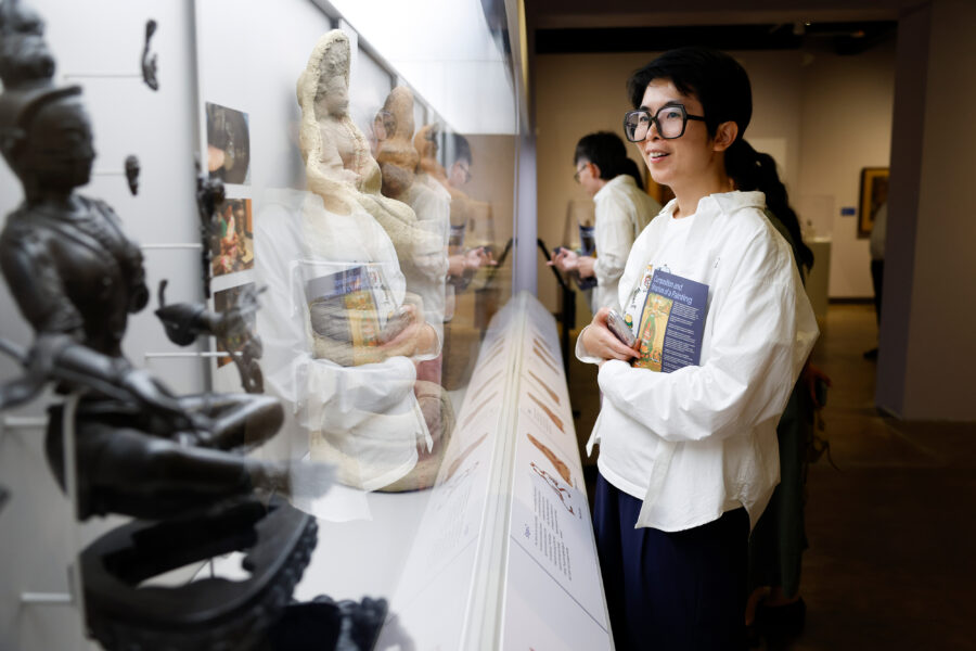 A smiling adult wearing glasses and a white button shirt looking at a glass case with sculptures