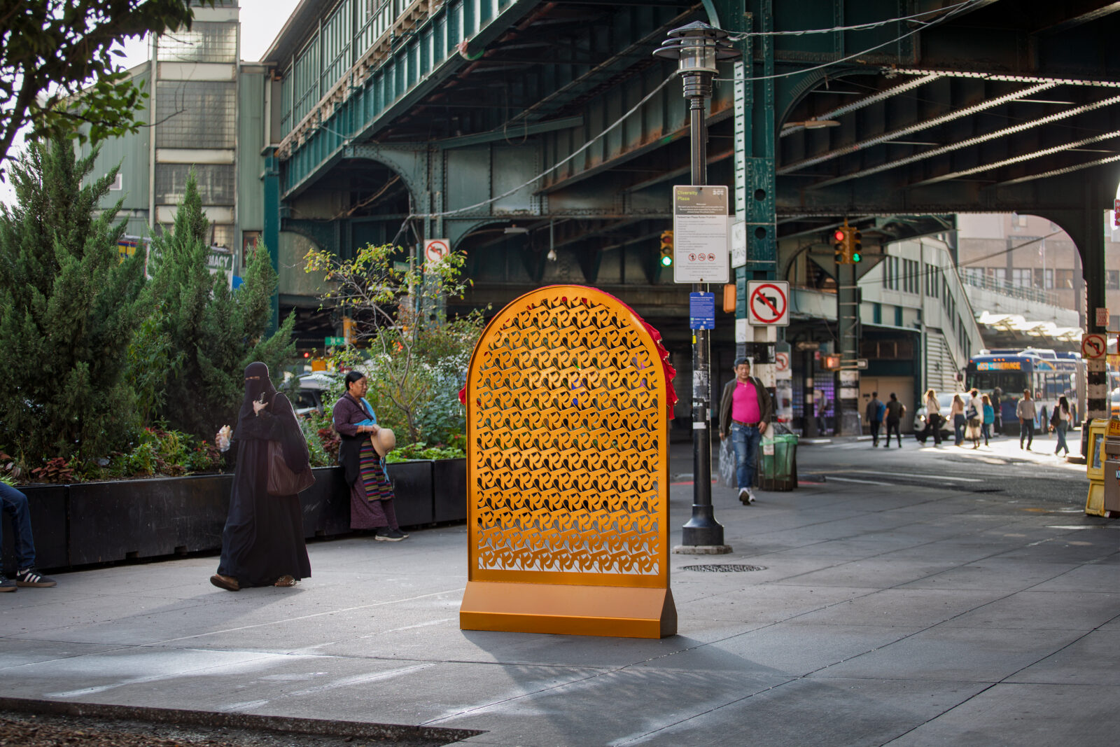 A gold arch made of repeating rows of ka, the first letter of the Nepali alphabet, near a green bridge with pedestrians walking nearby