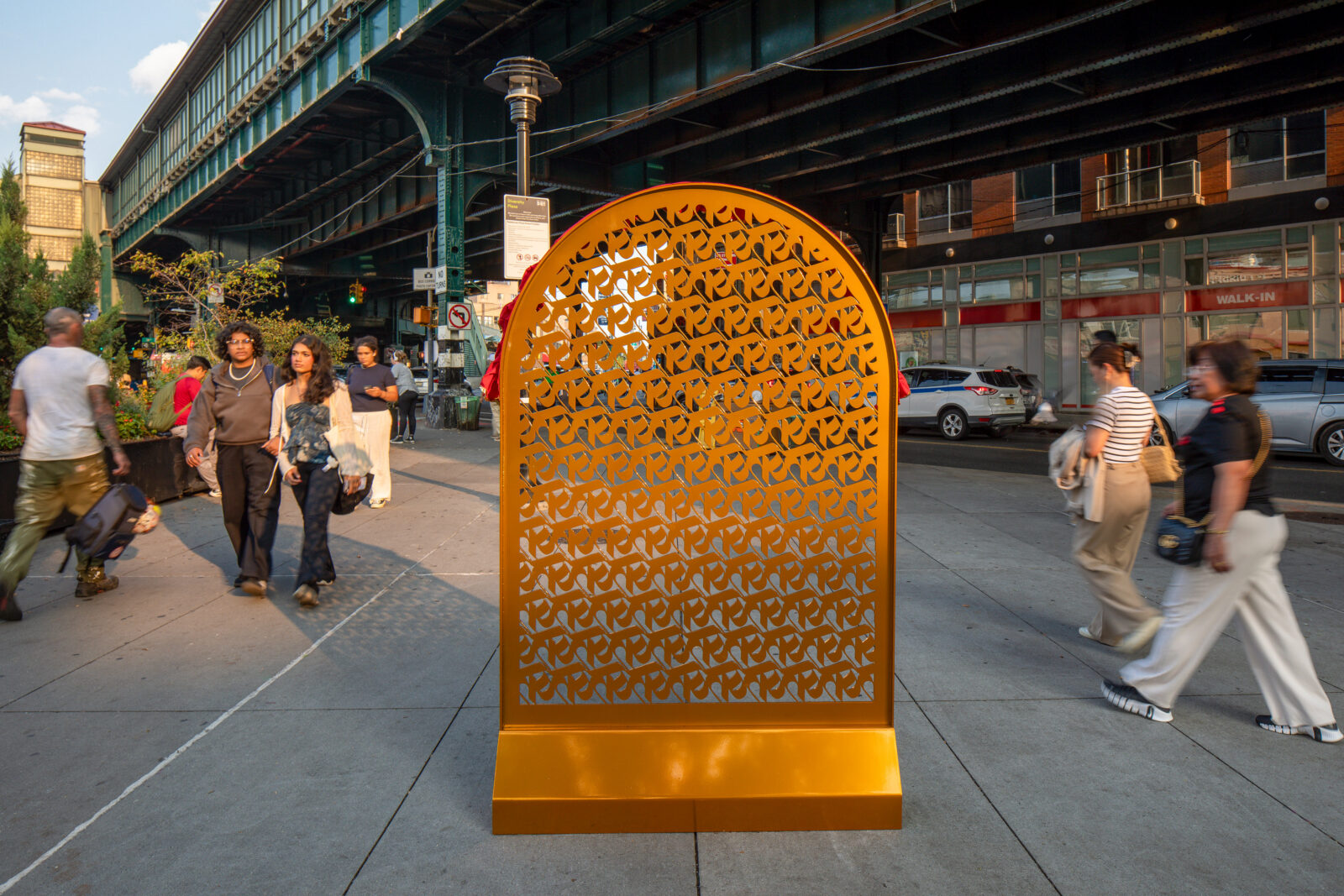 A gold arch made of repeating rows of ka, the first letter of the Nepali alphabet, near a green bridge with pedestrians walking nearby