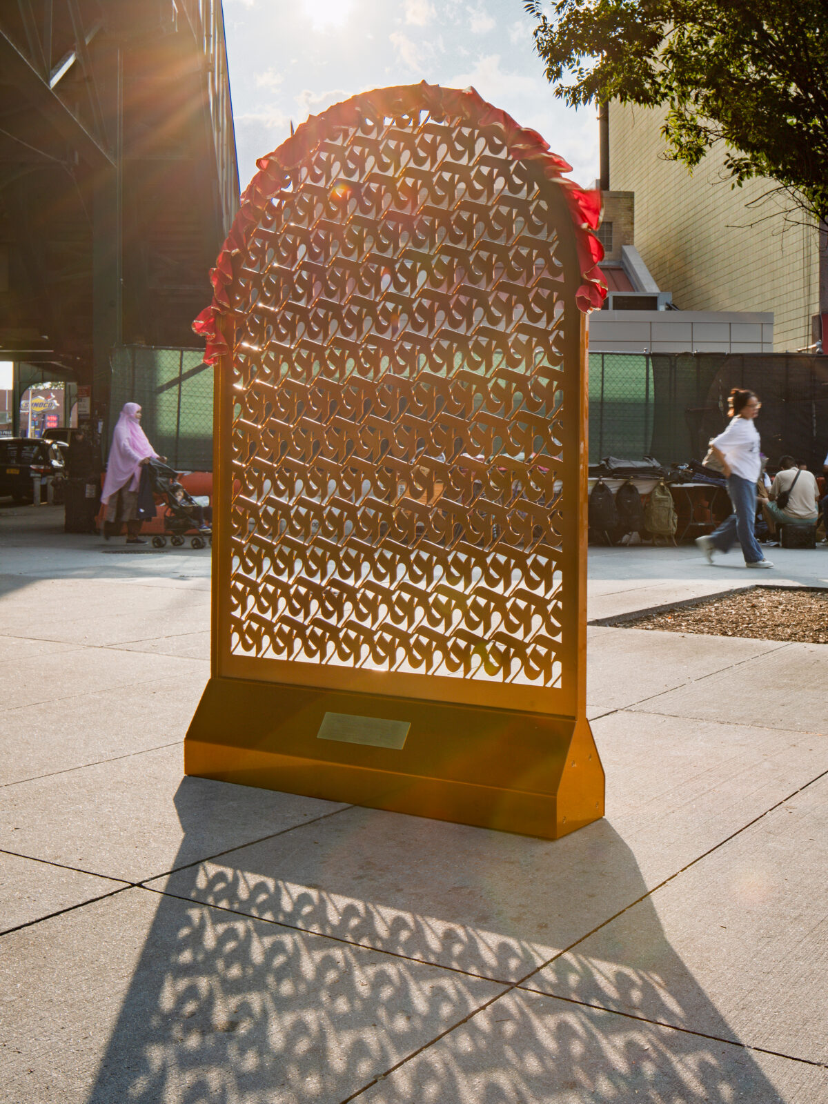 A gold arch made of repeating rows of ka, the first letter of the Nepali alphabet, with pedestrians walking nearby