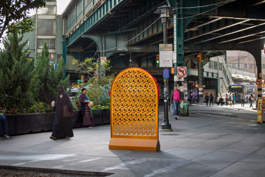 A gold arch made of repeating rows of ka, the first letter of the Nepali alphabet, near a green bridge with pedestrians walking nearby