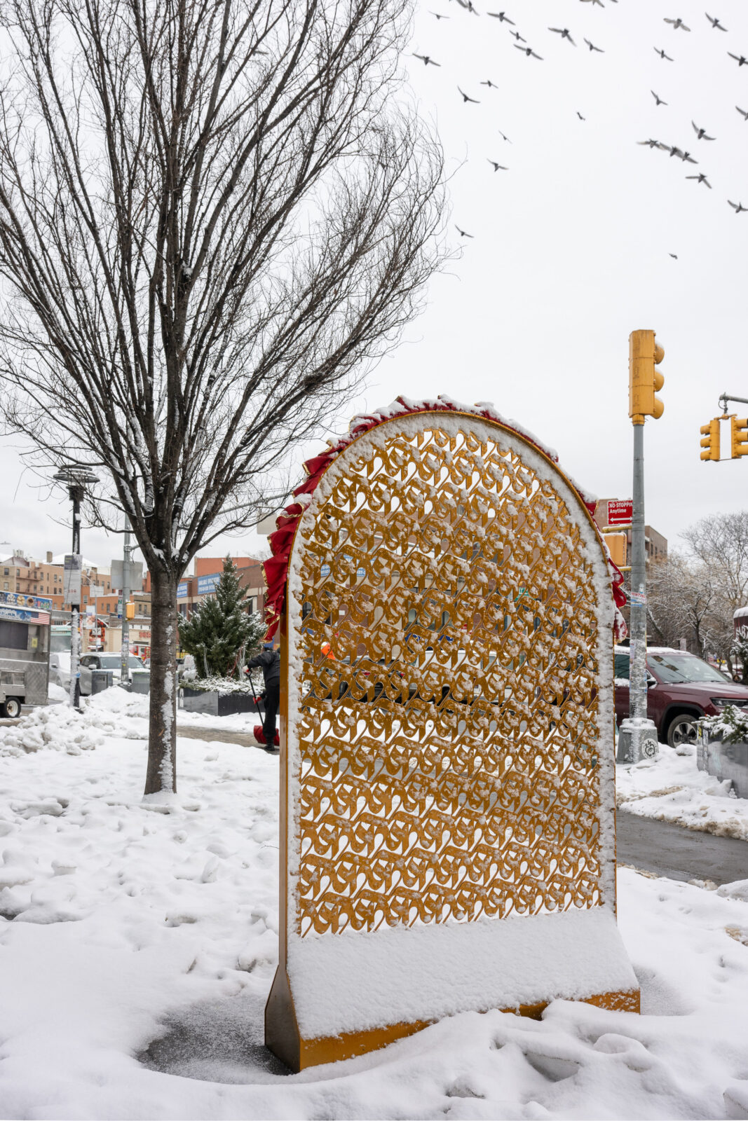 A gold arch made of repeating rows of ka, the first letter of the Nepali alphabet, in the wintertime with snow on the ground and the sculpture