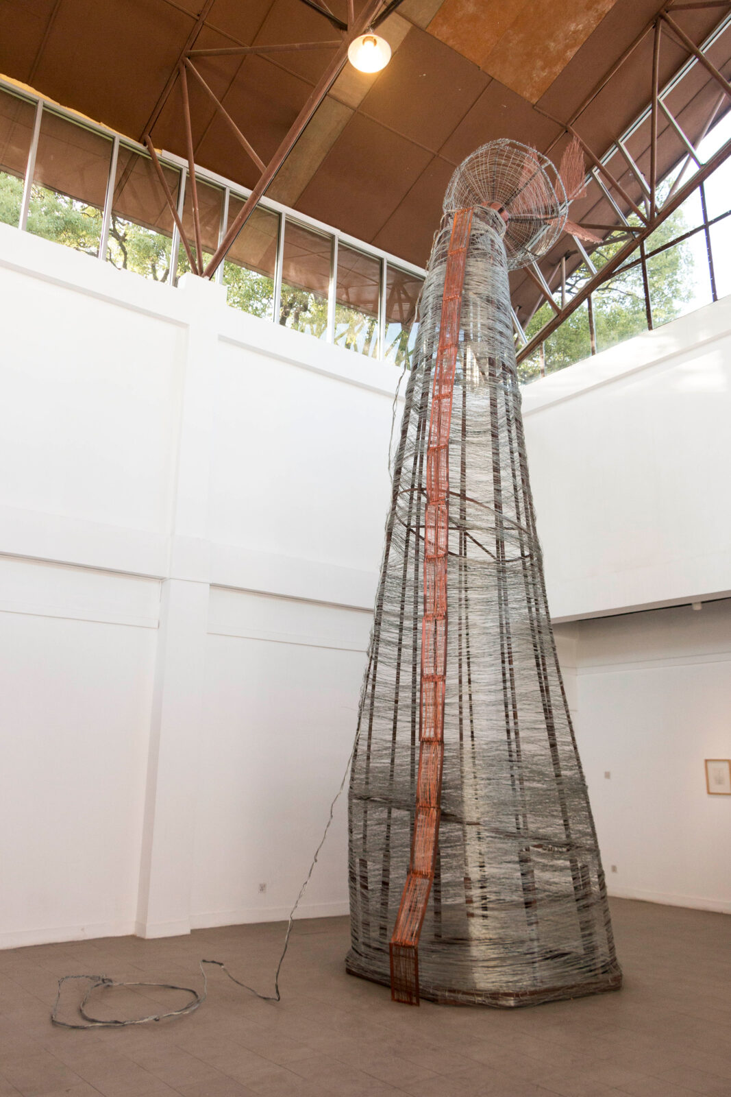 conical wire and rod sculpture extending from the ground to the ceiling