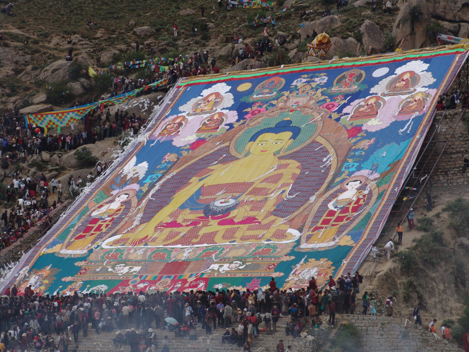Aerial photo of a crowd of people on a mountainside unfurling a large fabric banner that depicts a deity