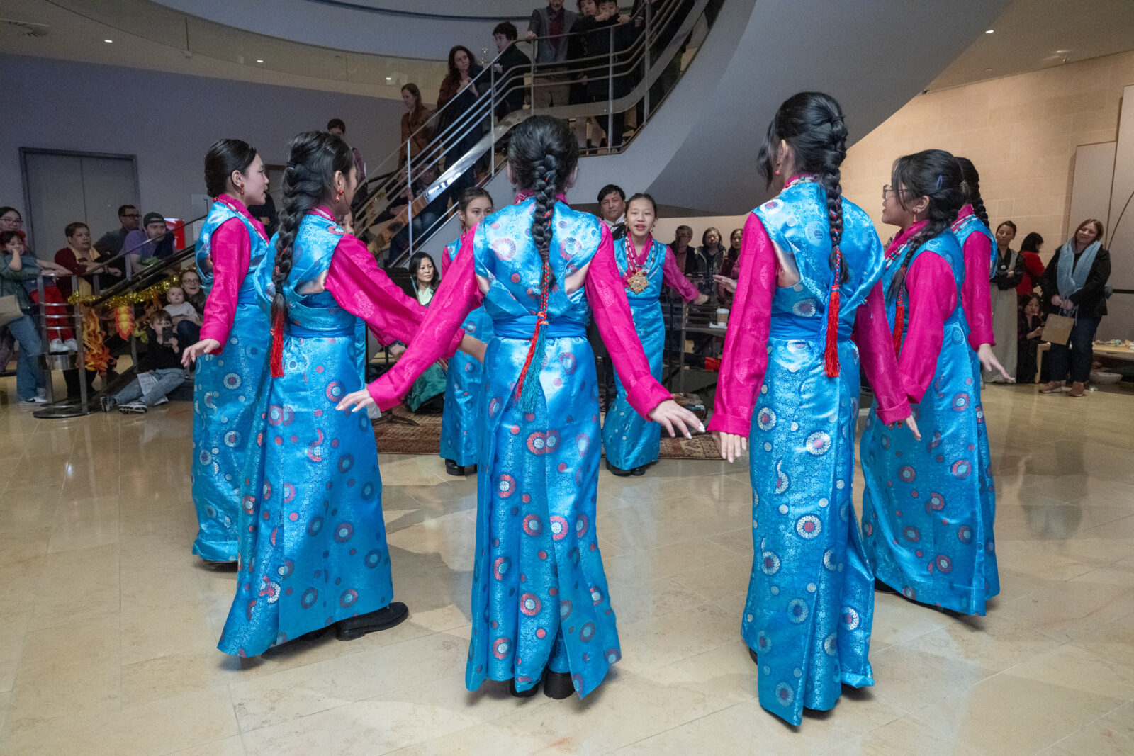 group of dancers dressed in blue stand in a circle, holding hands in the Rubin Museum lobby