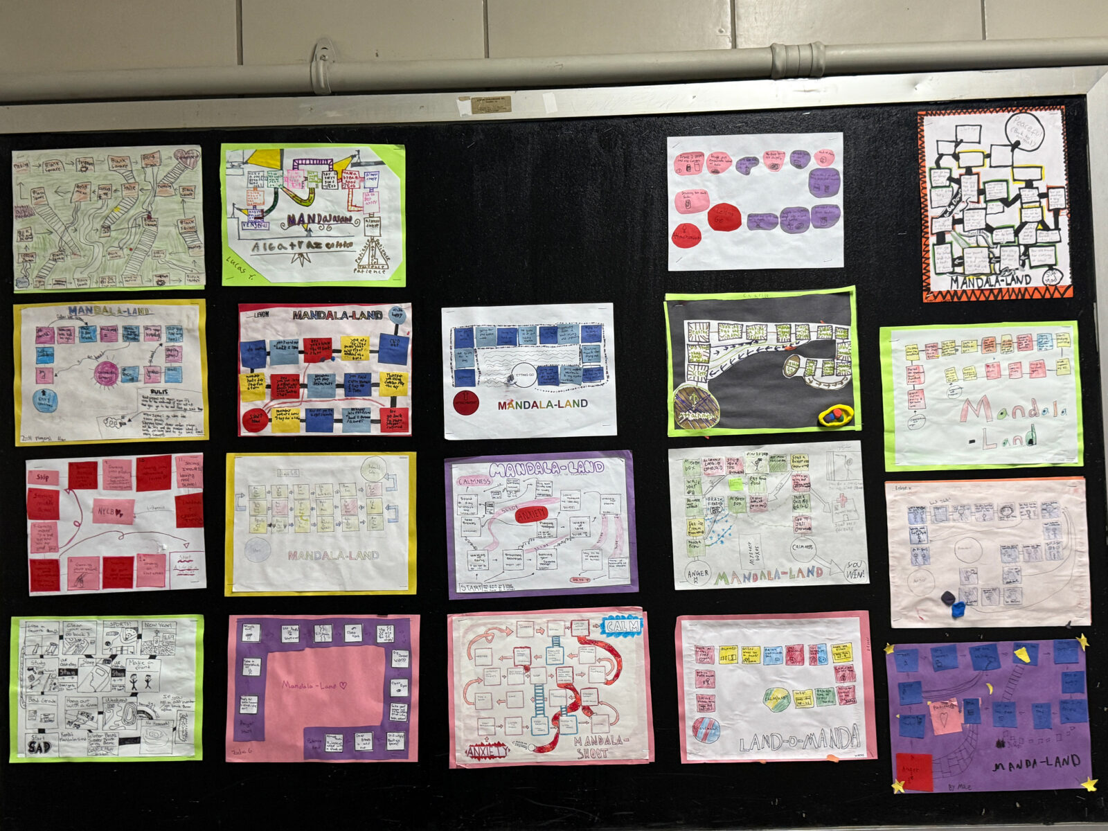 a blackboard displaying a grid of nineteen board games created by students arranged in rows of five