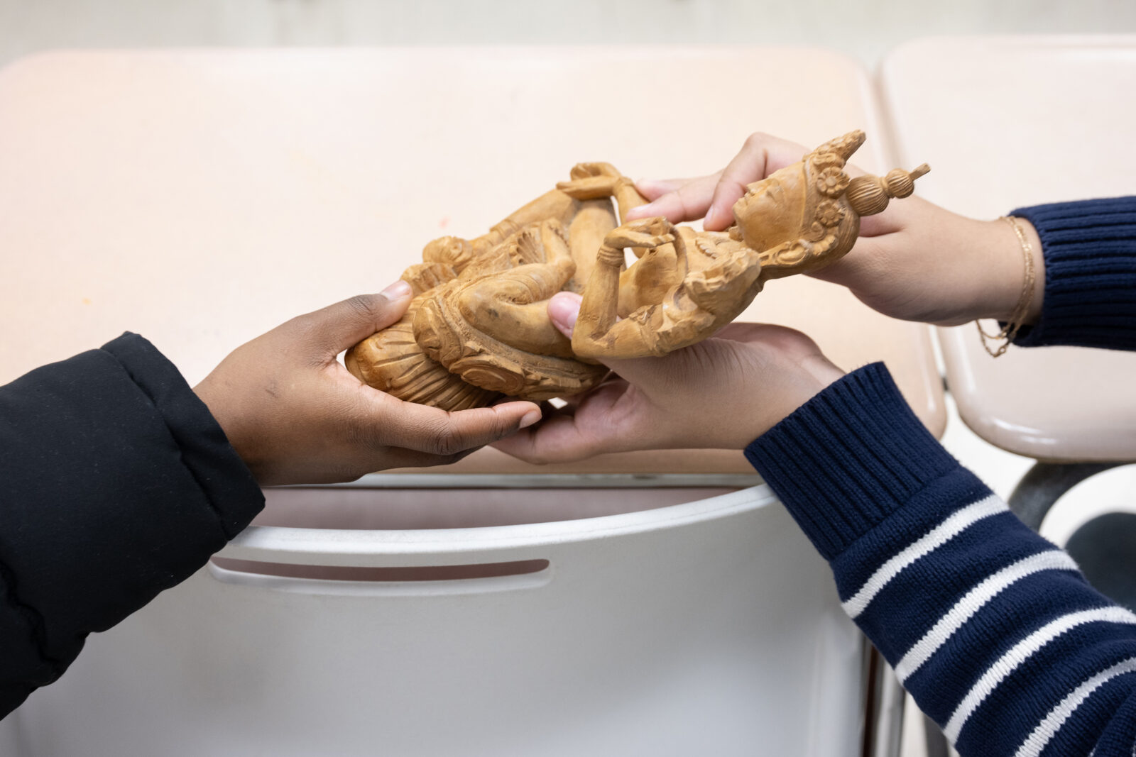 A close up of two people's hands holding a small wooden carved figure