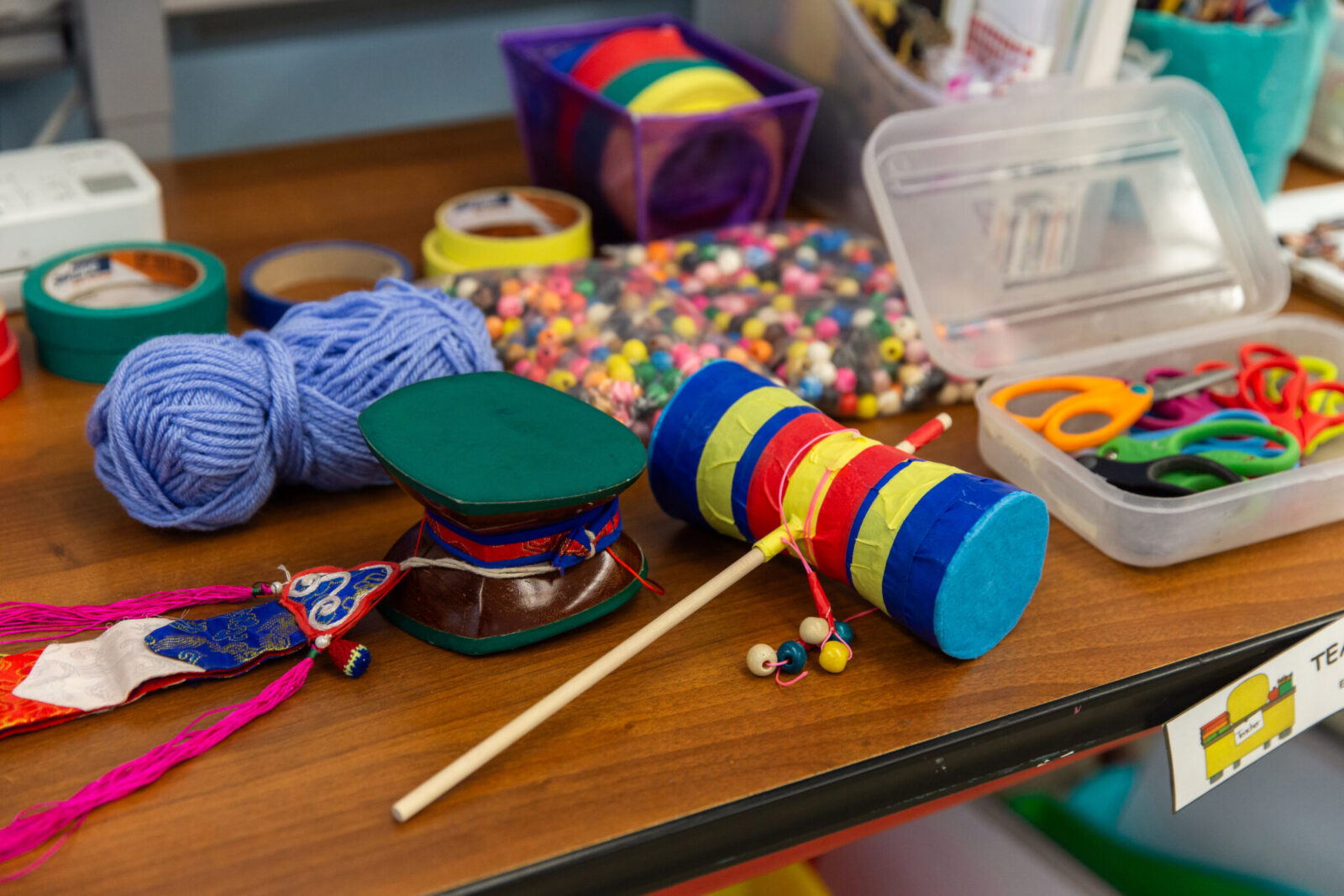 a handmade drum resting on a desk beside various art supplies