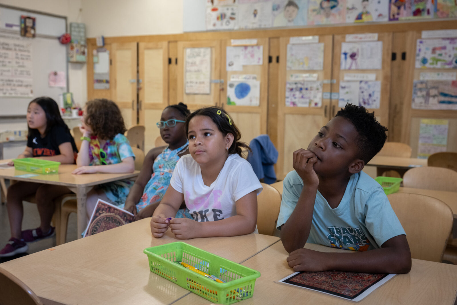 Five students sit at desks in a classroom, looking off to the side