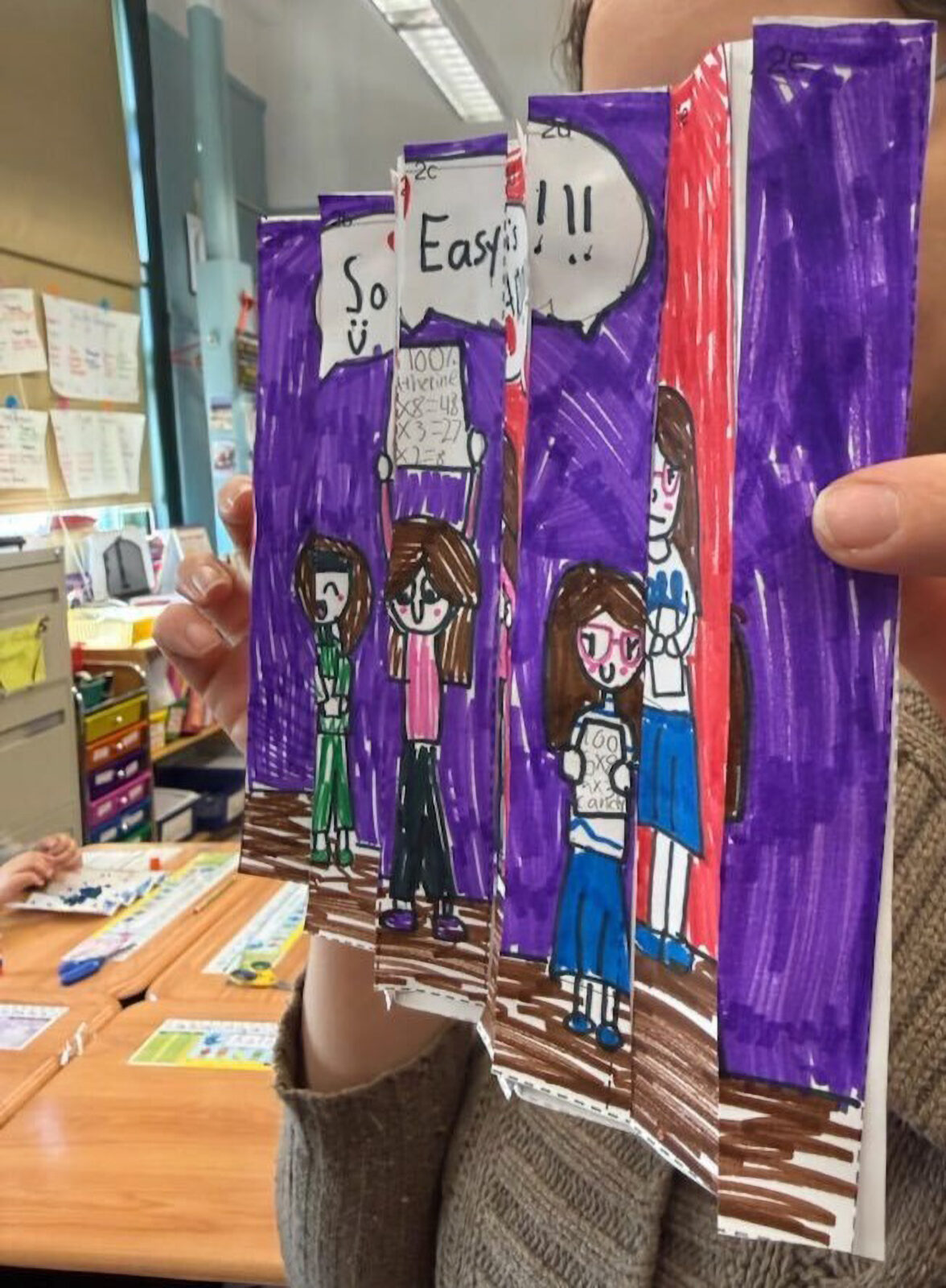 a student holding up a sheet of paper folded like an accordion, displaying a drawing across the panels