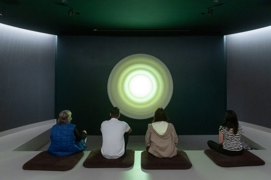 Four people sitting cross-legged in front of a glowing sculpture by Palden Weinreb.