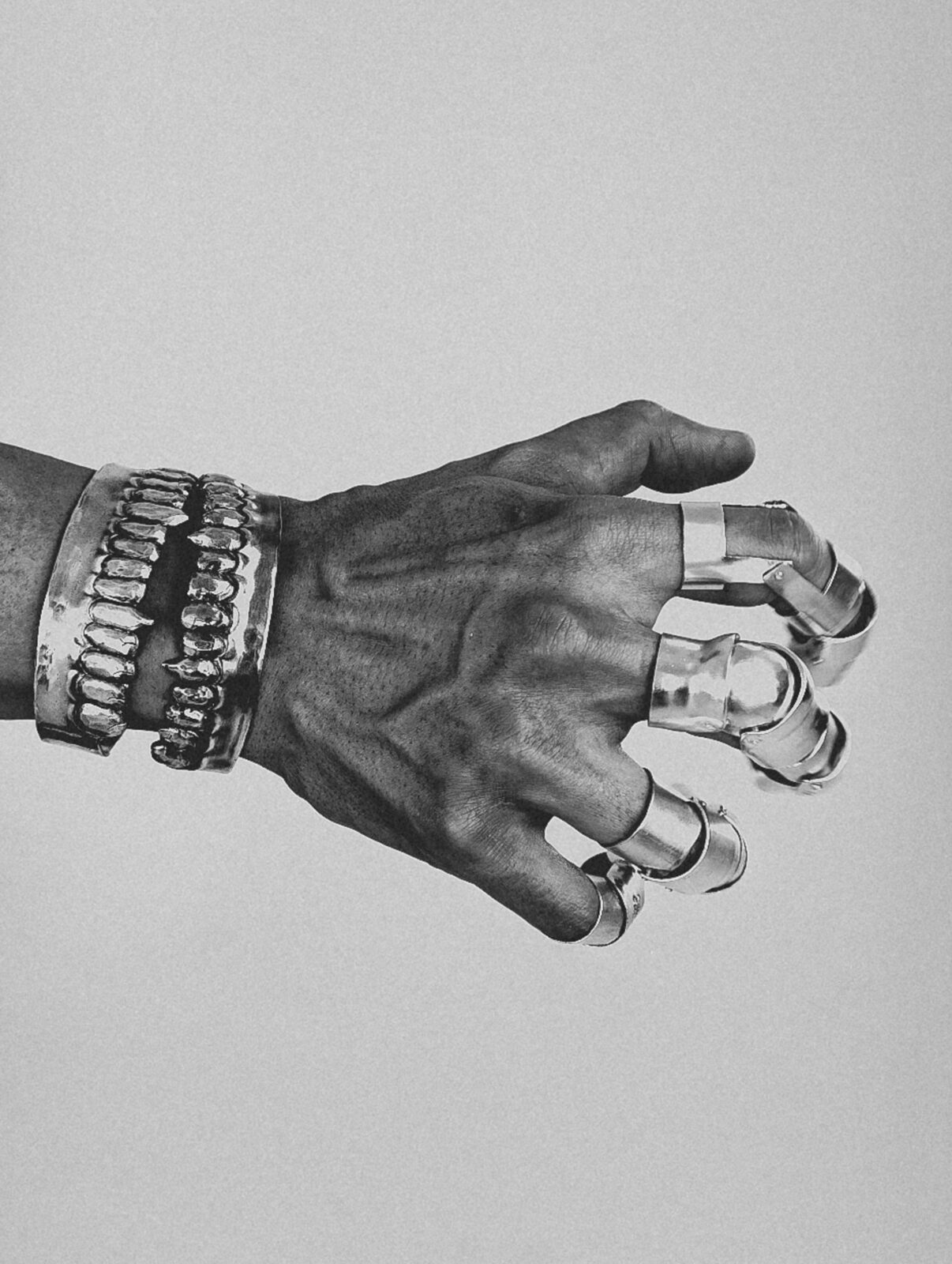 Black and white photo of a right hand wearing multiple rings and two bracelets in the shape of human gums and teeth