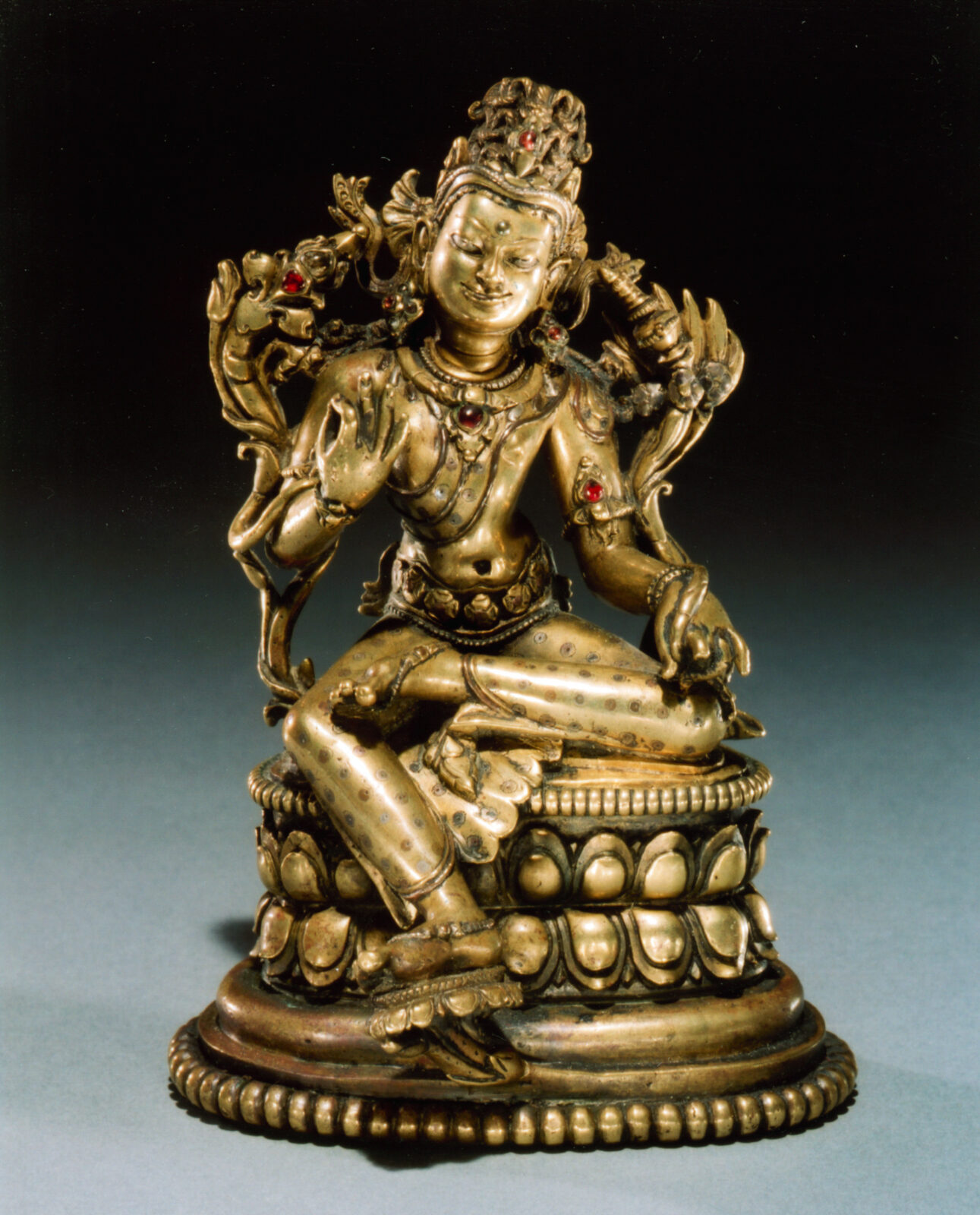 Golden statue of bejeweled figure seated on lotus blossom.