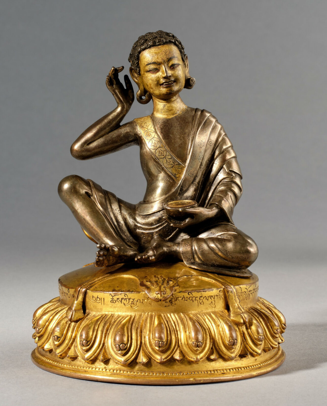 Golden statue of male figure seated on lotus blosson.