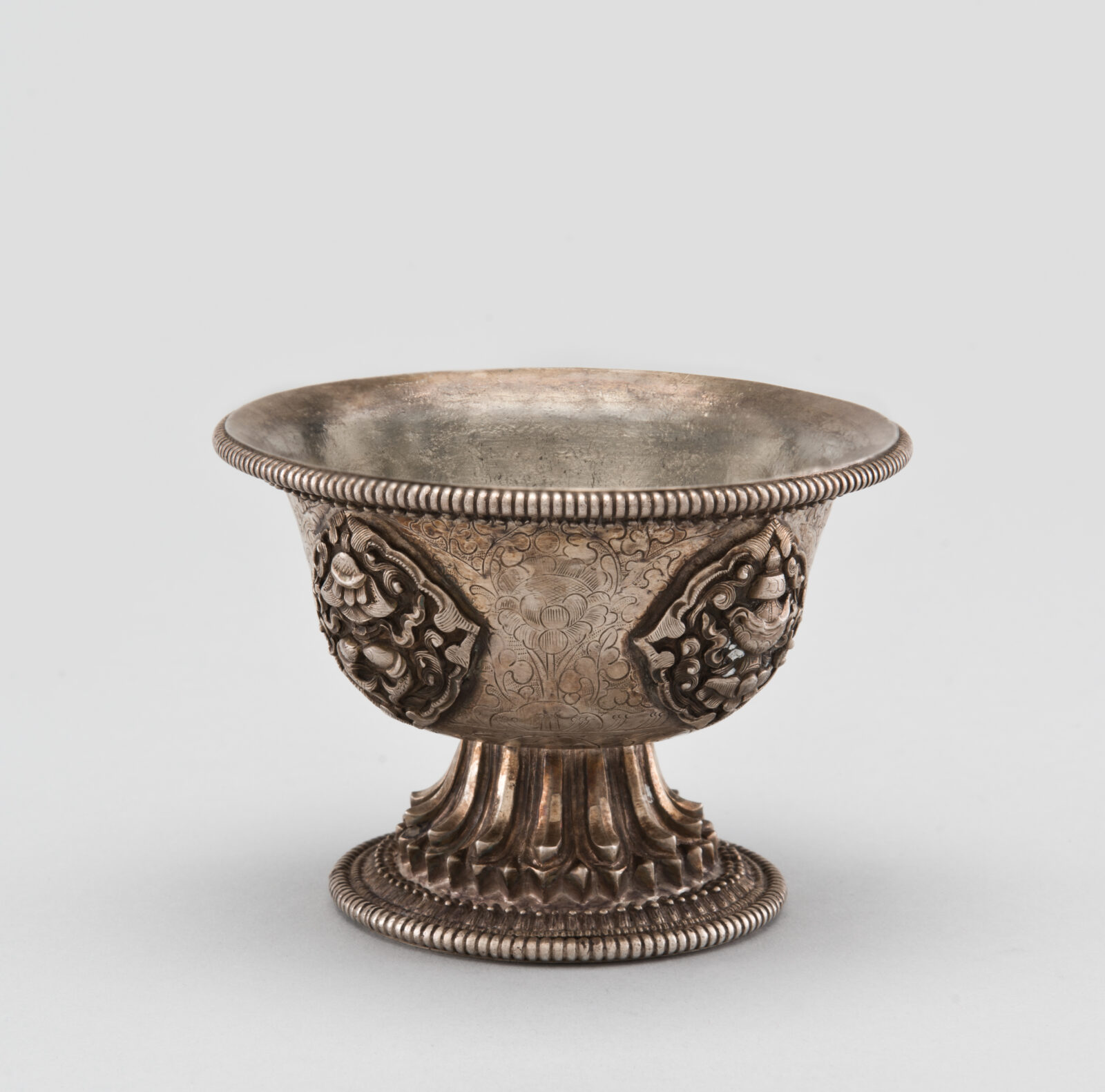 Ornately carved metal cup on lotus pedestal.