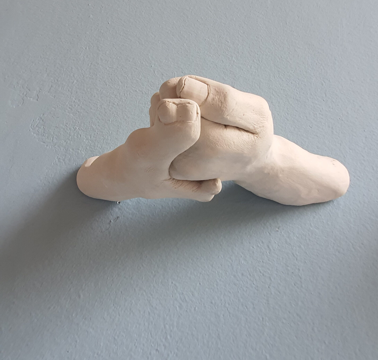 sculpture of white hands holding each other, extending from the wall. One thumb has two nails.