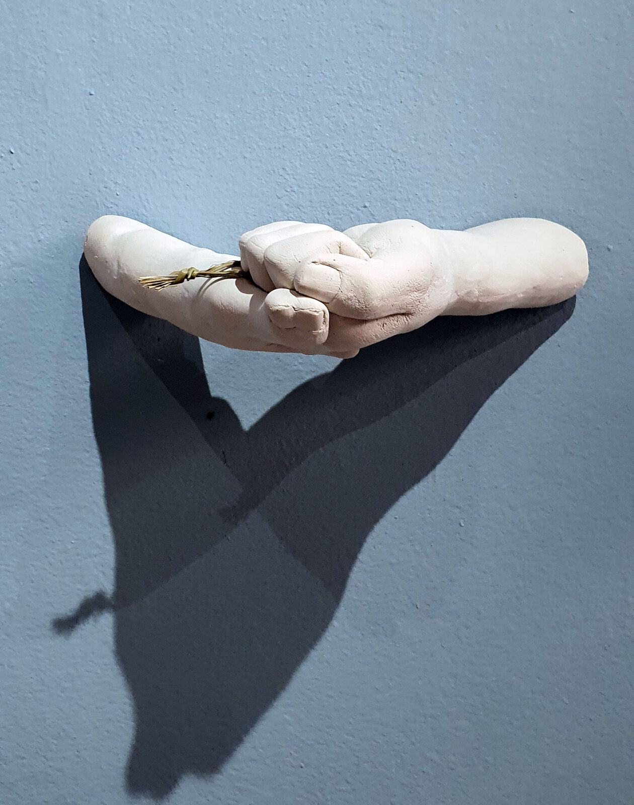 sculpture of white hands holding each other, extending from the wall. Straw peeks out from between the hands.
