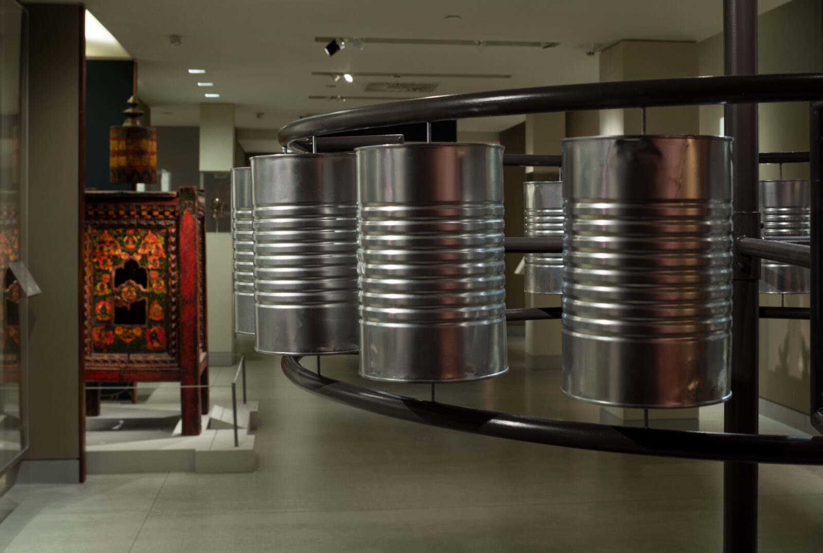 sculpture of tin cans welded to a circular metal form, mounted on a central metal pole in a gallery