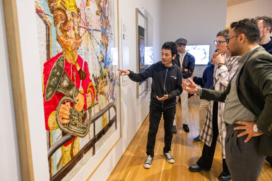 Artist standing in front of painting, pointing and explaining the artwork to visitors