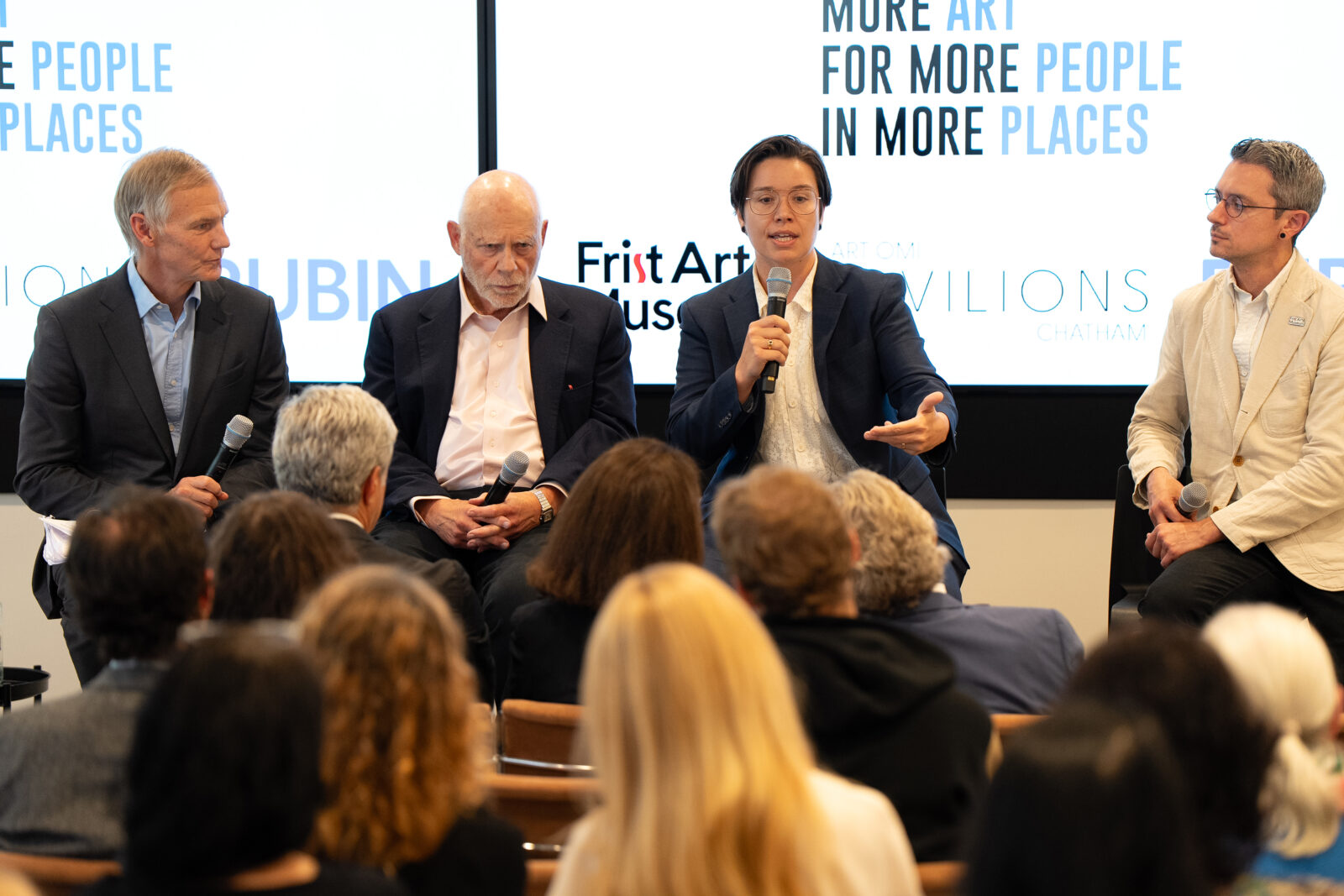 Jamie Lawyer sits with three other museum leaders in front of an audience. Behind them is a white backdrop displaying the slogan "MORE ART FOR MORE PEOPLE IN MORE PLACES".
