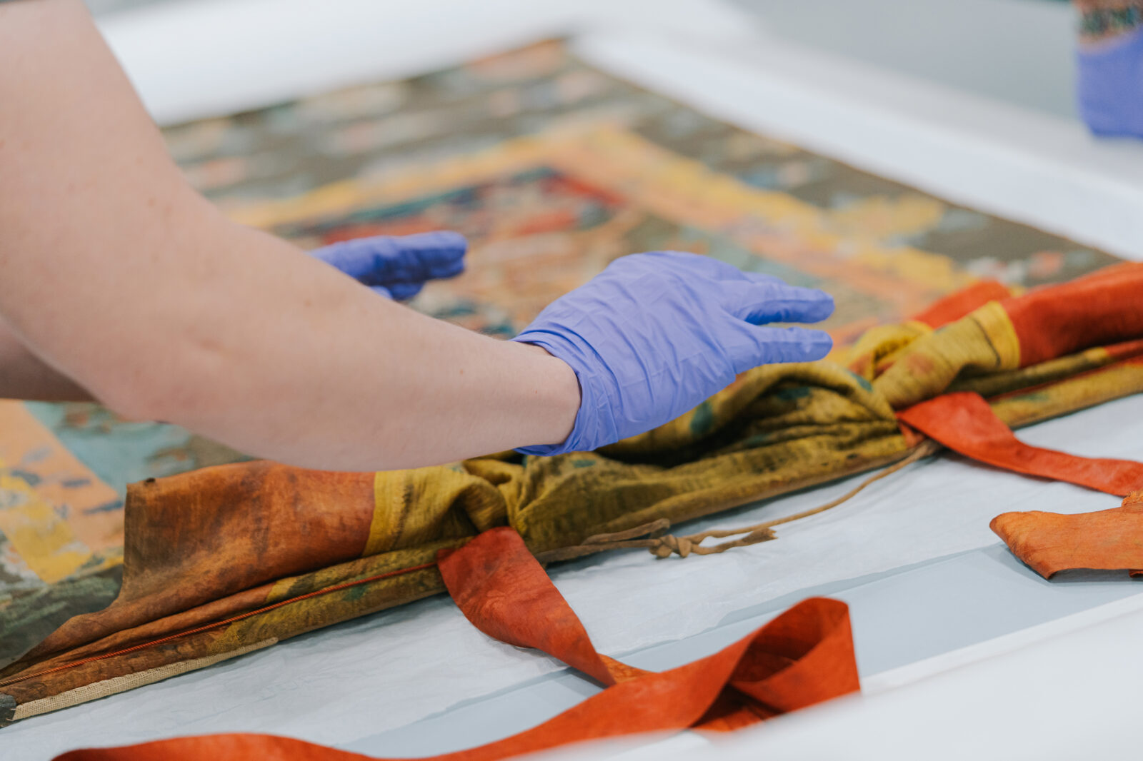 Gloved hands hover over a painting laid flat on a table