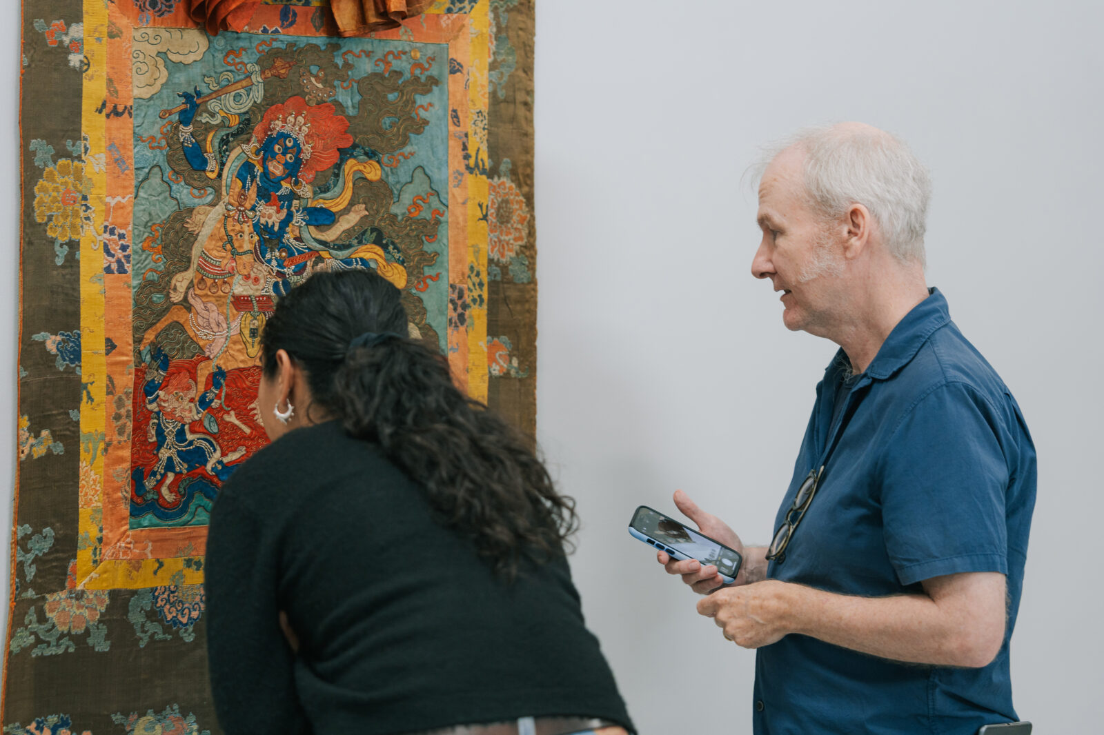 An adult woman with brown curly hair and an older man with grey hair lean in to look closely at a painting of Padmasambhava