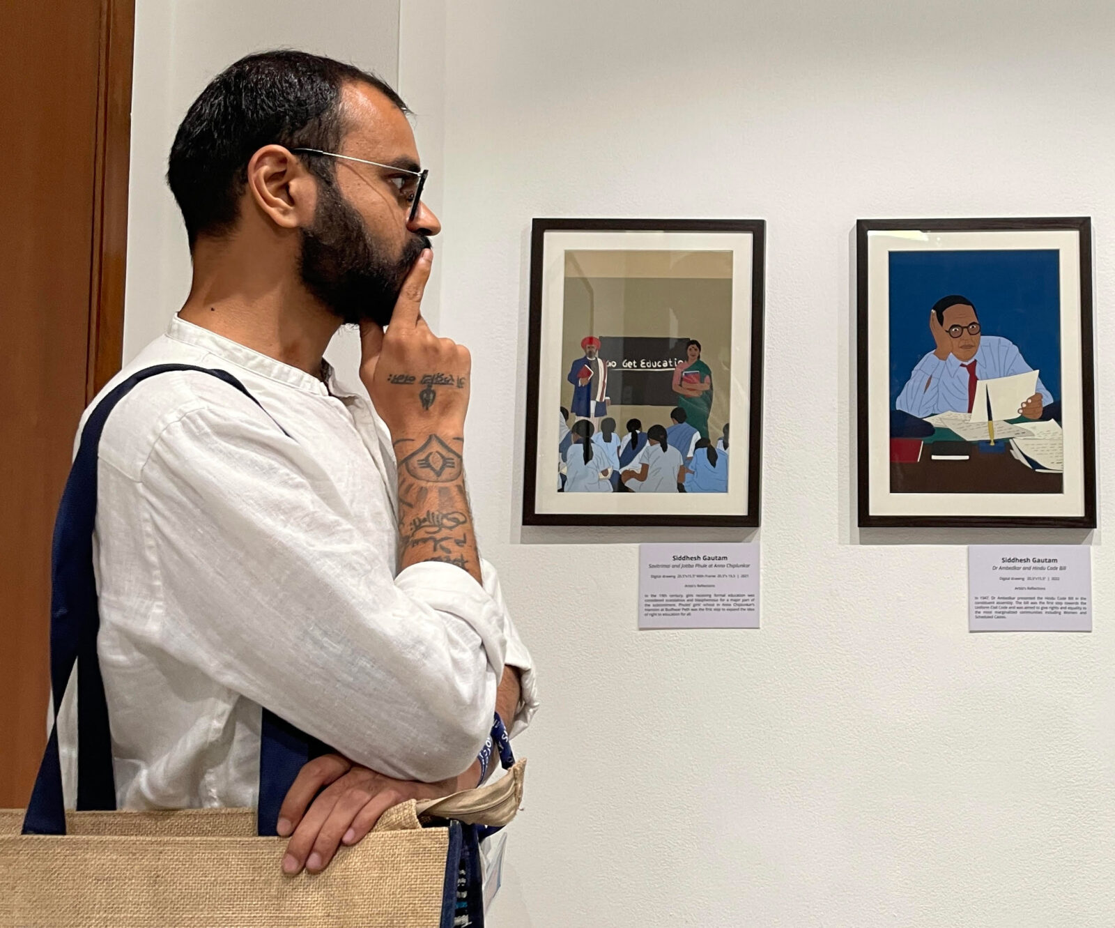 man looking at framed photos hung on a white wall, with his hand on his chin