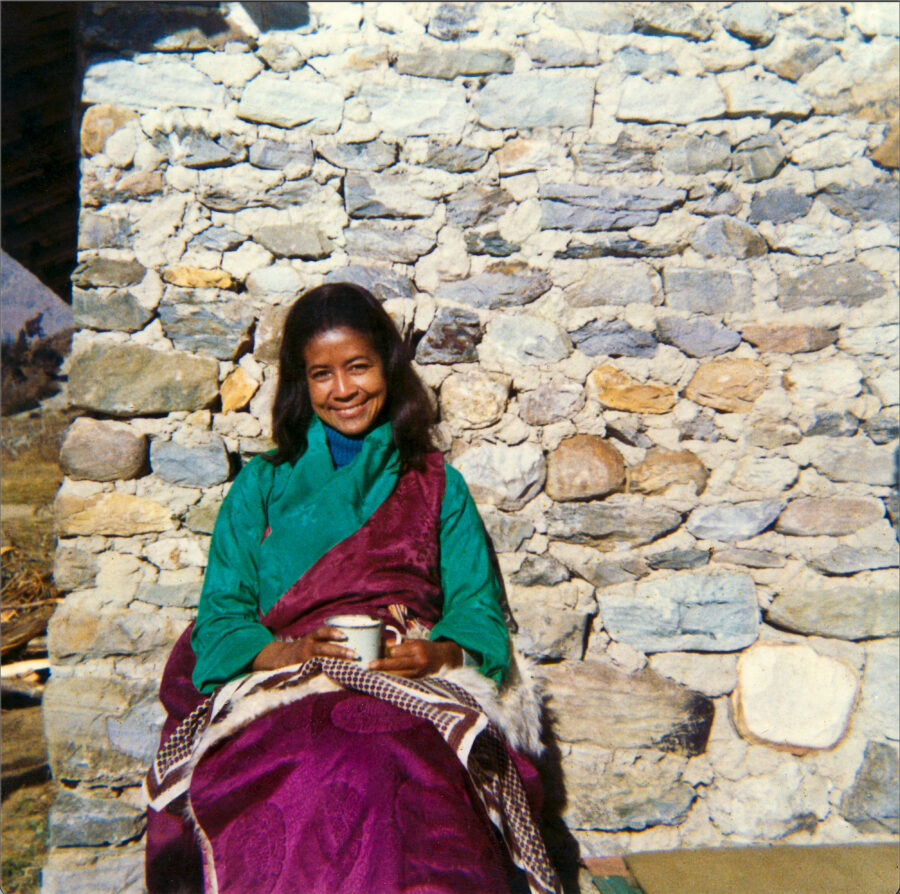 sister max sitting on a bench smiling with a stone wall behind her