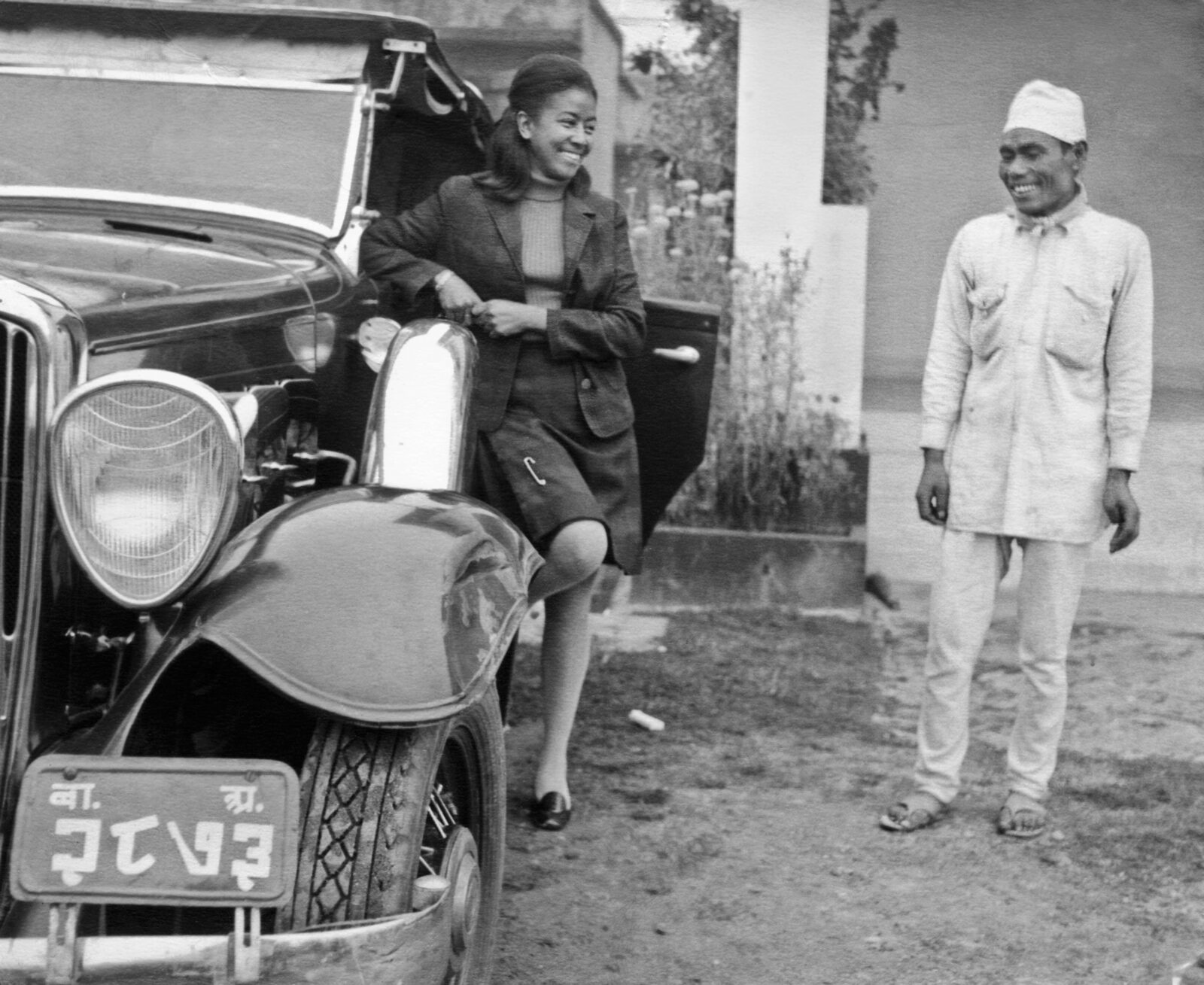 black and white photo of sister max leaning on a convertible, smiling